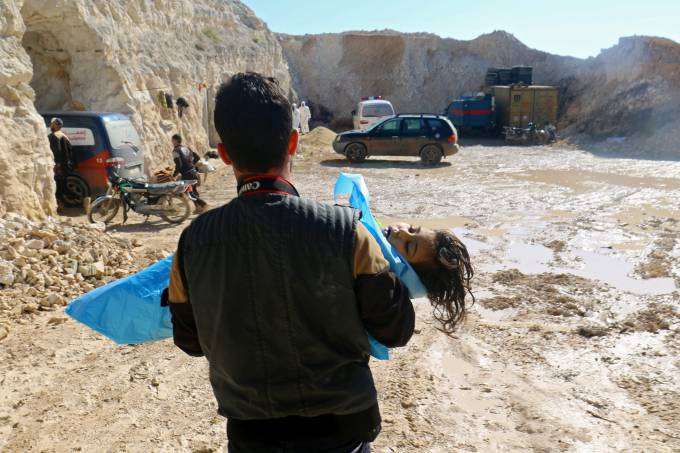 Homem carrega criança após ataque com gás na cidade de Khan Sheikhoun